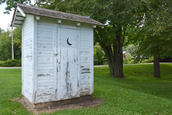 A white outhouse located in the back of the farmstead