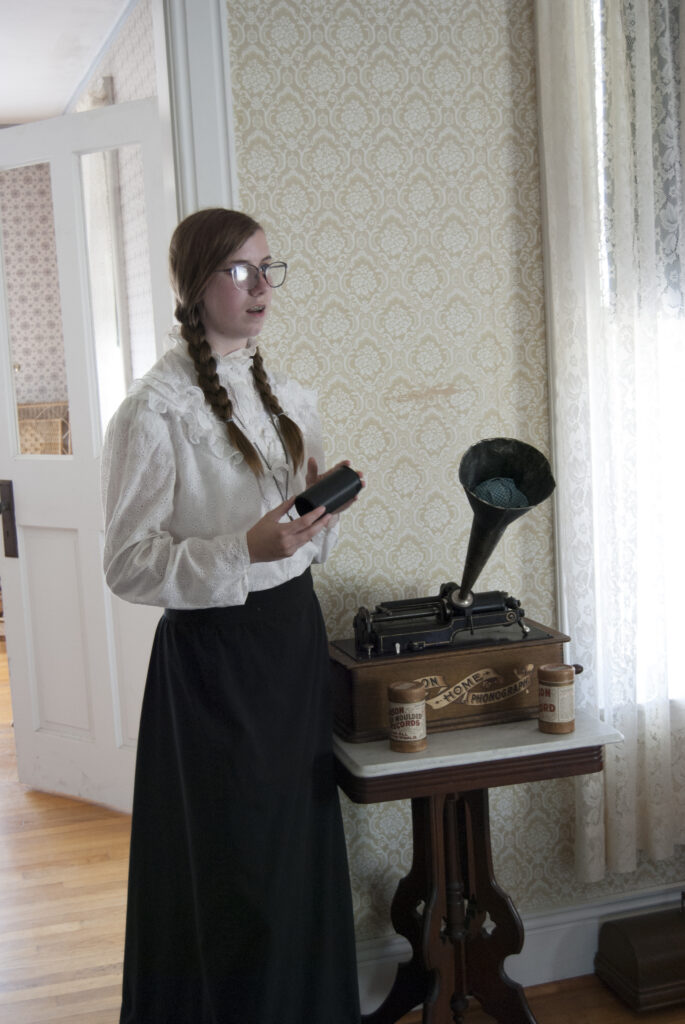 A woman wearing period clothes gives a talk to guests in side a building at Stonefield during her employment. 