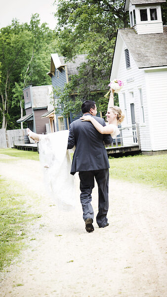 A husband carrying his wife, in her wedding dress, bridal style away from the camera