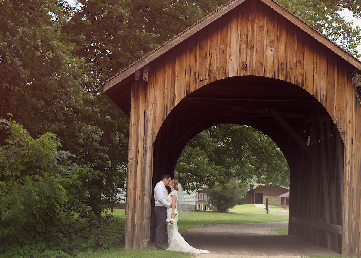 A newly wed couple kissing underneath a wooden archway