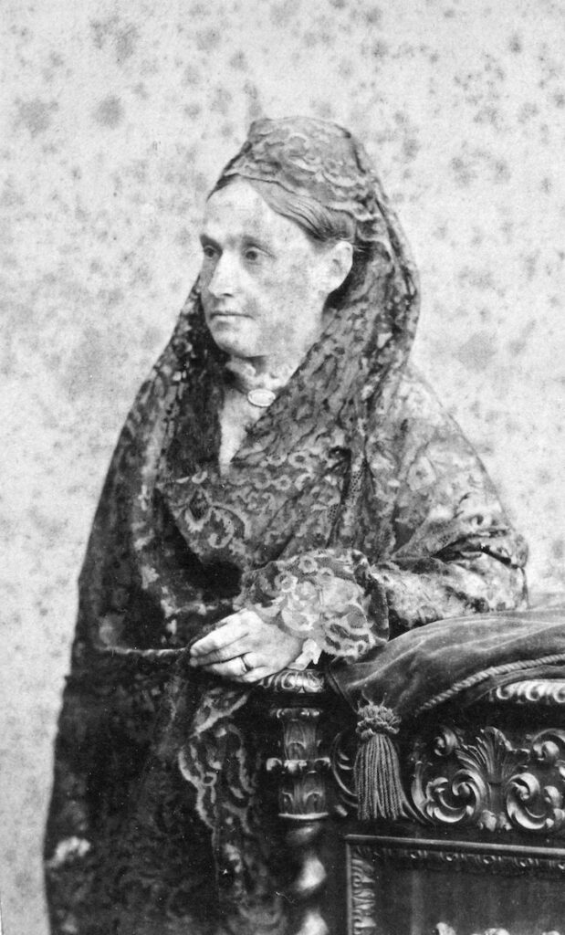 Catherine Dunn Dewey standing with her left forearm on a bedframe
